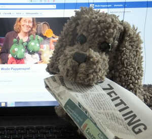 Stoffhund mit Zeitung im Mund, im Hintergrund ein Computer mit der geöffneten Facebookseite von Wodo.